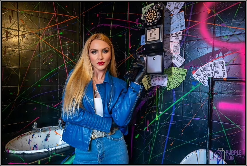 A performer in a blue leather jacket beside a sticker-covered vintage payphone