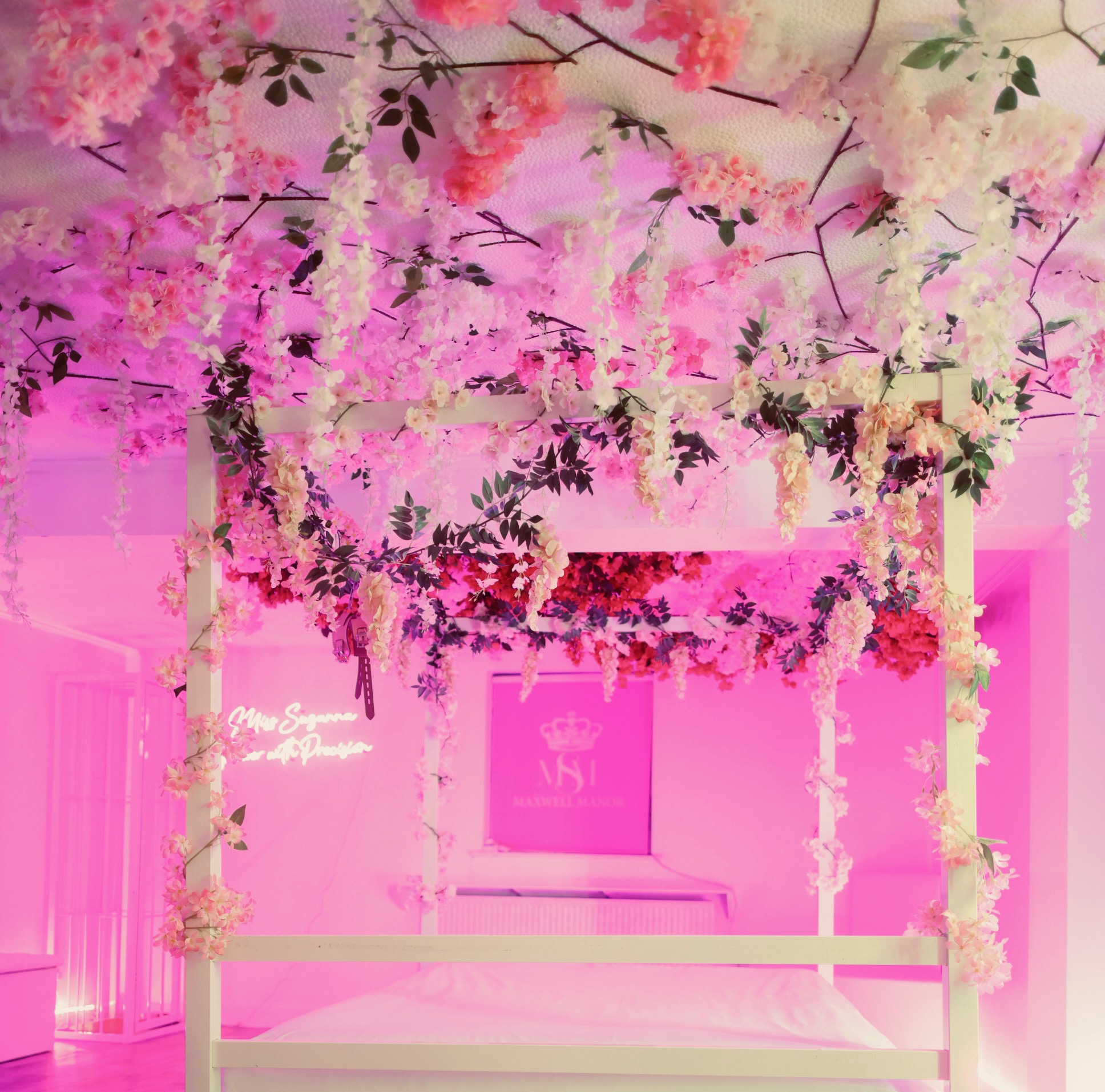 The Enchanted Forest under hot pink light, its white four-poster frame dressed in cherry blossom and trailing wisteria